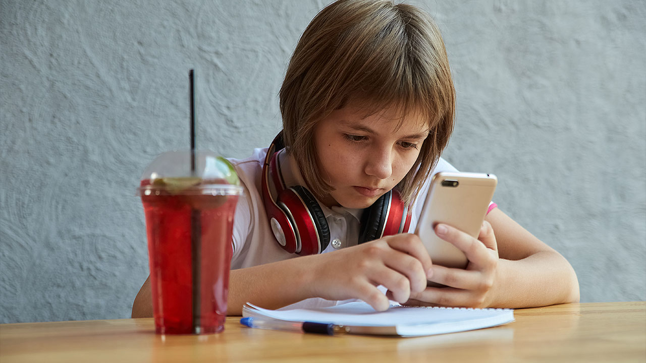 Čo znamená bolesť chrbta na rôznych miestach? 4 Školák sedí za stolom zhrbený nad mobilným telefónom.